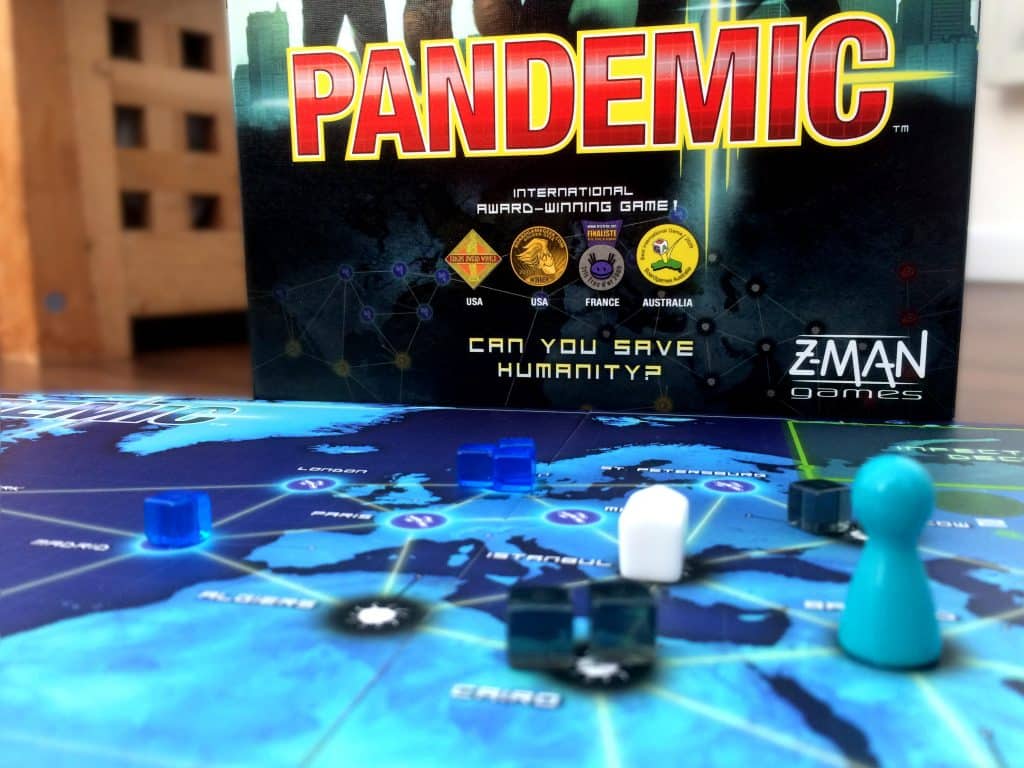 the Pandemic game board with a number of components in the foreground and the game box in the background