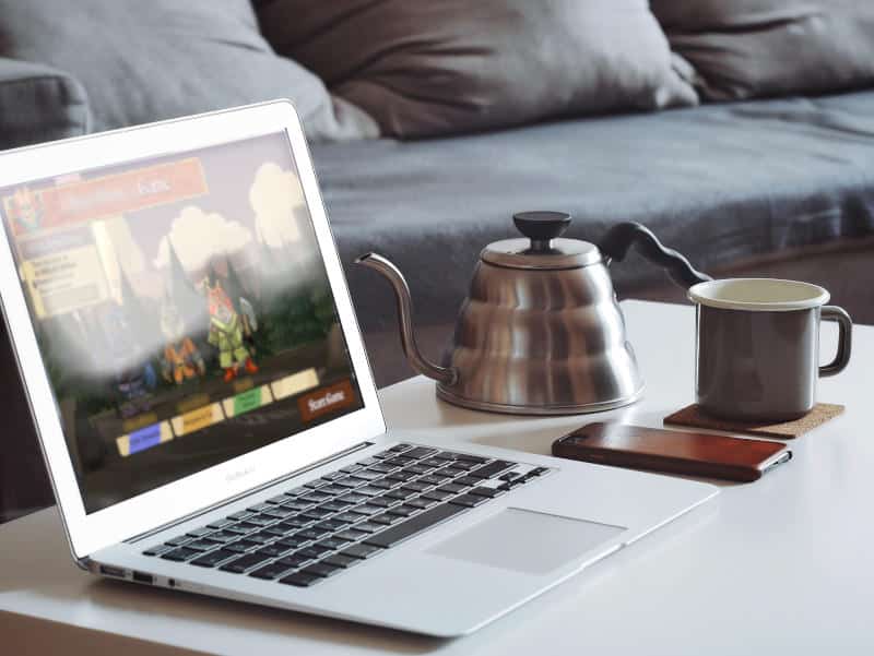 a laptop on a coffee table showing the digital version of the game Root, next to a small tea pot and a mug (Photo by Goran Ivos on Unsplash)