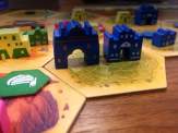 some of the wooden components representing buildings of different types and some of the cardboard hexagonal tiles making up the terrain