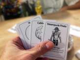 a hand holding three cards from the game, with a small "Oscar" in the background