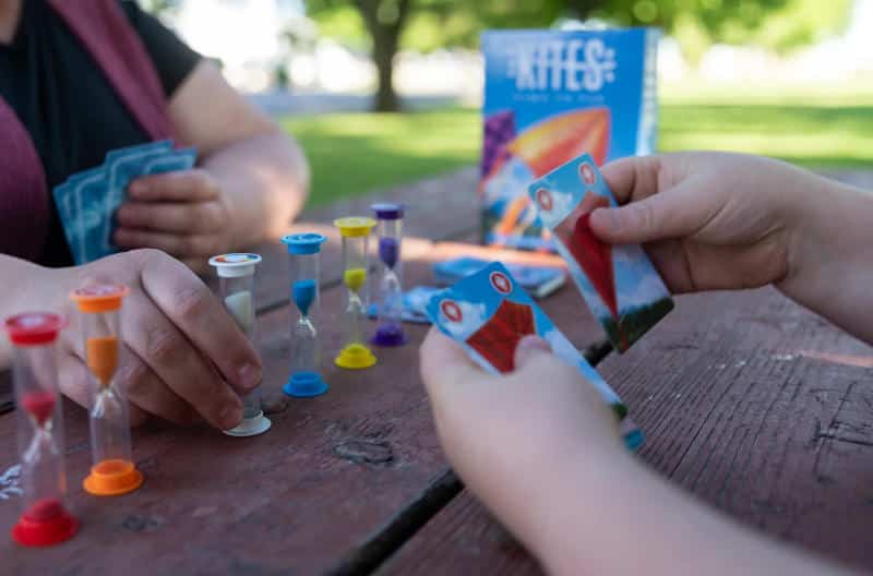 a number of coloured sand timers and two people playing the card game Kites (Photo courtesy of Floodgate Games)