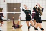 two female volleyball players in black sports kits high-fiving each other, while one player of the opposing team is lying on the floor