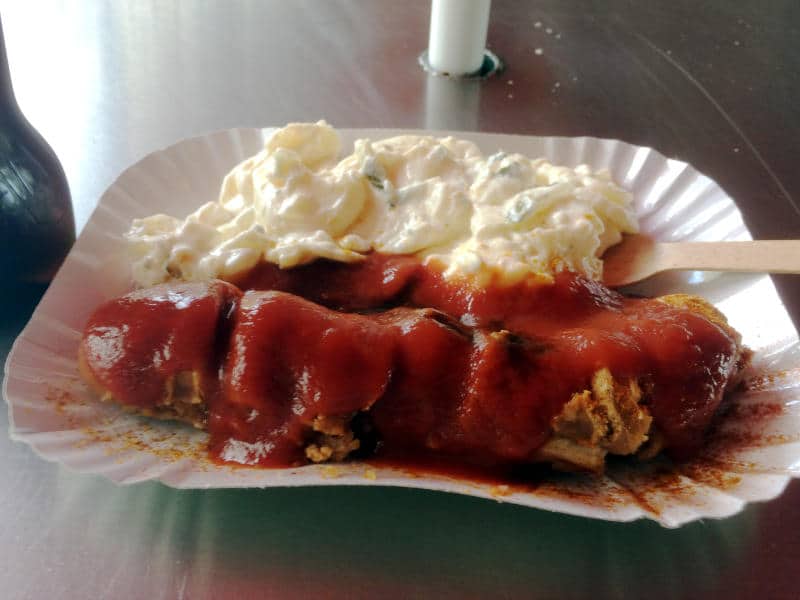 a Berlin Currywurst, a fried pork sausage covered in ketchup mixed with curry powder, accompanied by potato salad with mayonnaise