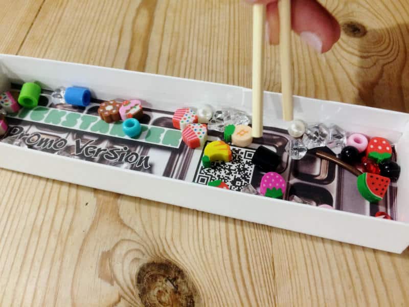 a box full of small plastic beads, plastic gems, small erasers and similar and a pair chopsticks